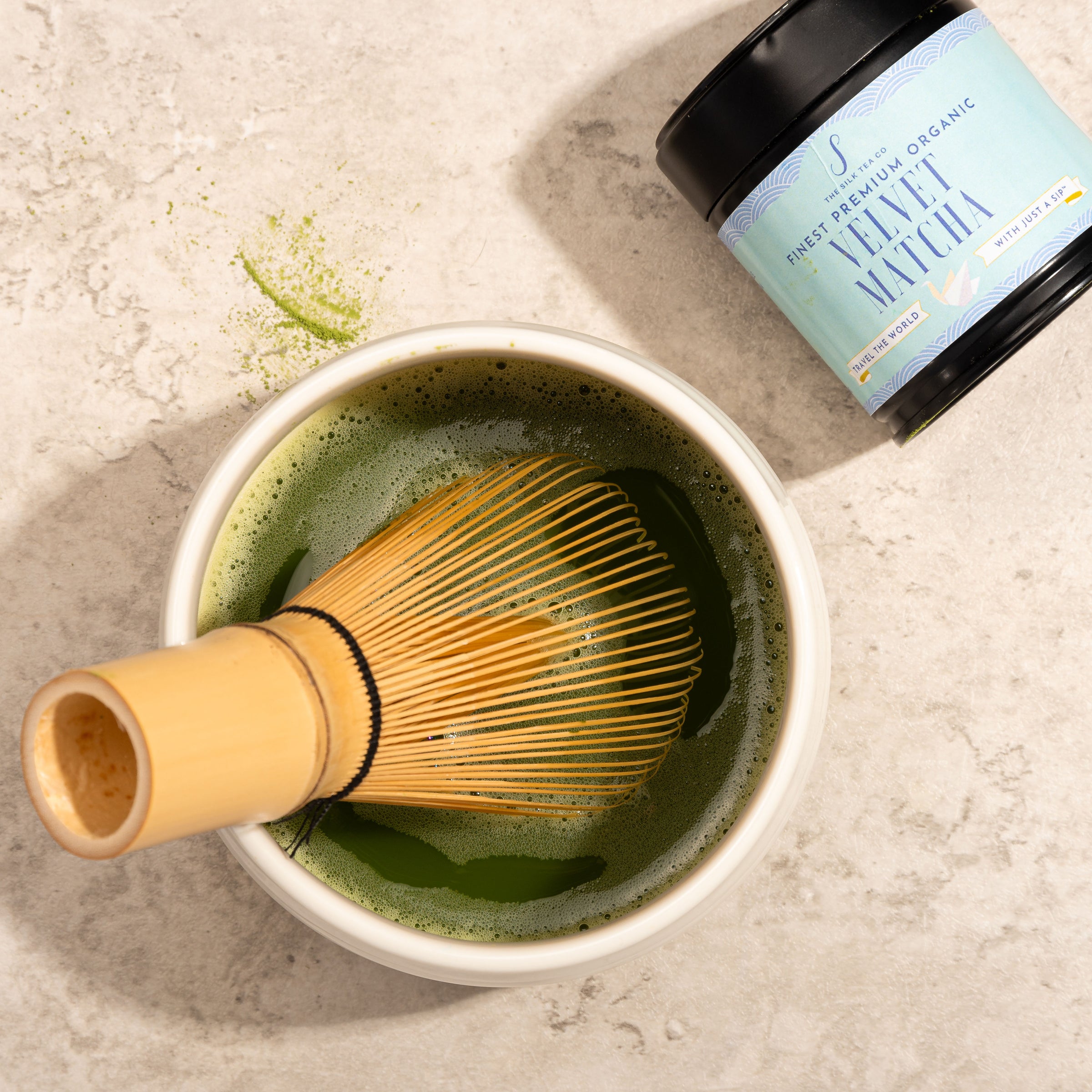 Chasen Japanese matcha whisk in a ceramic bowl with organic matcha and the tin of the product